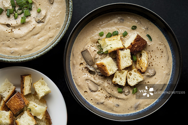 两碗奶油蘑菇汤，配有烤面包丁和切碎的葱花图片素材