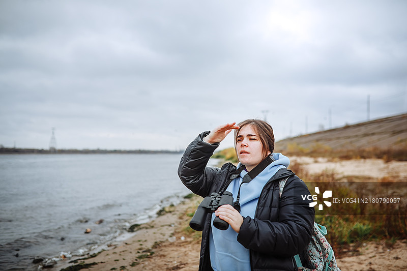 观鸟爱好者，穿着保暖的女士在水边用双筒望远镜观鸟图片素材