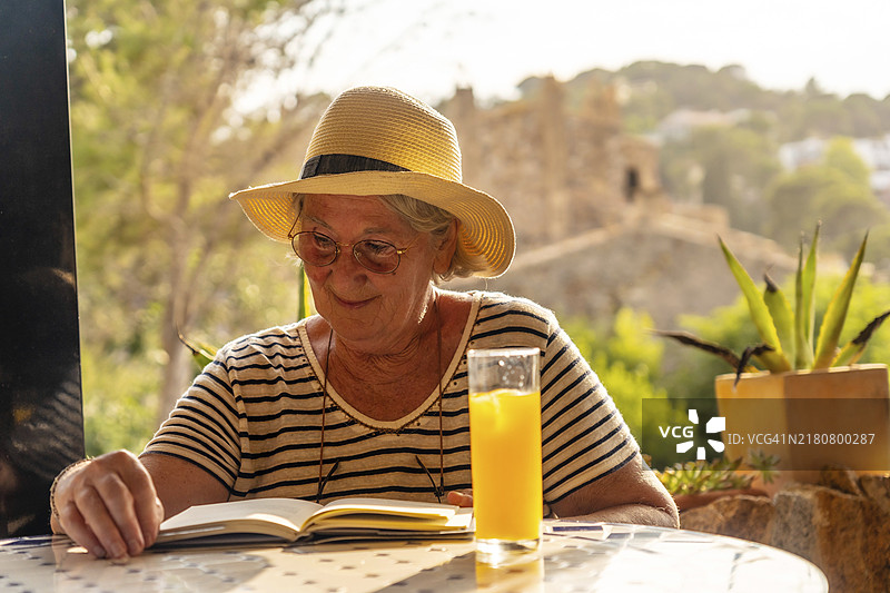 快乐的老年妇女在户外露台上阅读书籍，欣赏自然风光图片素材