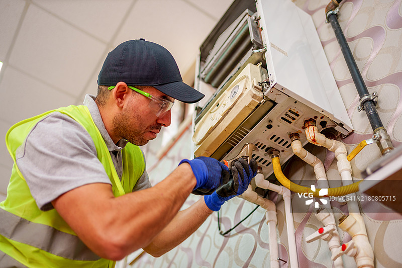 身穿绿色背心和帽子的技术员正在检修壁挂式锅炉的内部组件图片素材