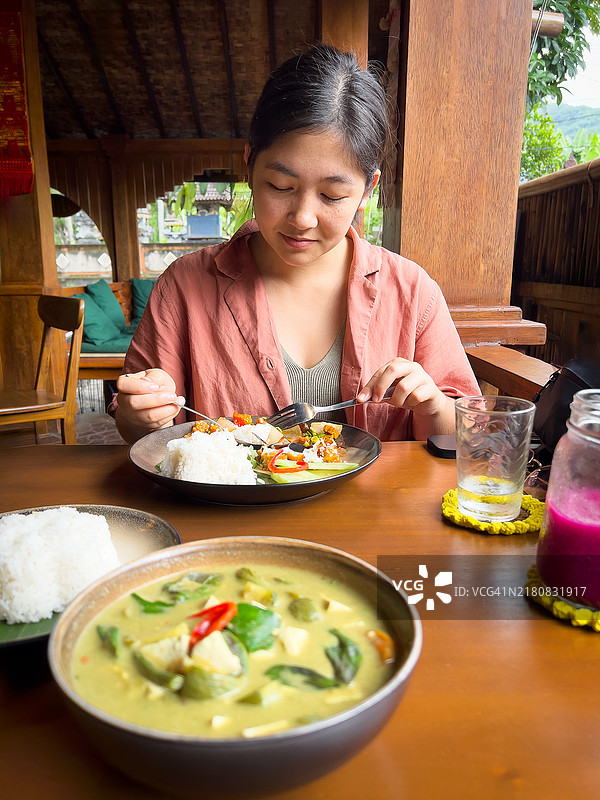在餐厅里吃泰国和印度尼西亚素食的混血年轻女人图片素材