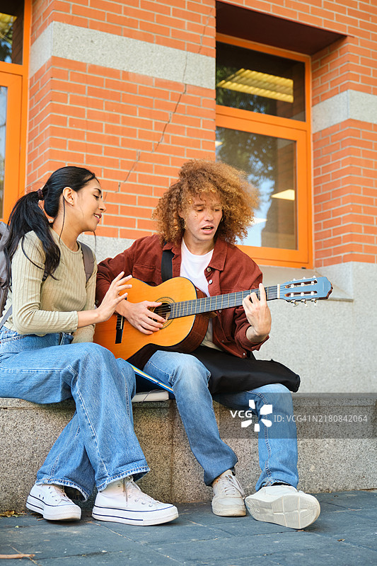 年轻人为户外就座的女子弹奏吉他图片素材