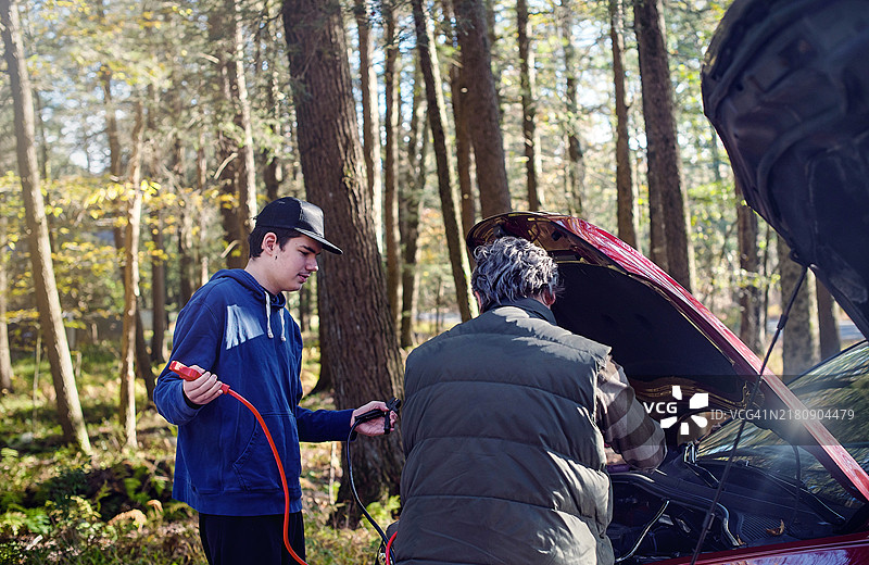 在森林中启动车辆：中年男人指导患有自闭症的青少年进行汽车维护基础图片素材