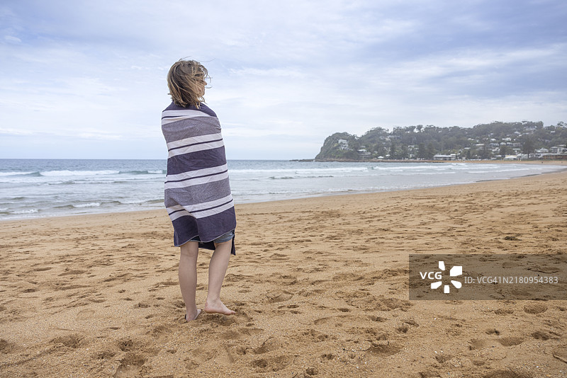 背影的少女站在海滩上，裹着毛巾。图片素材