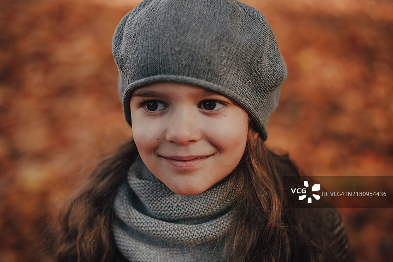 戴着灰色贝雷帽的棕眼女孩，4-5岁，背景是秋天的树叶。图片素材