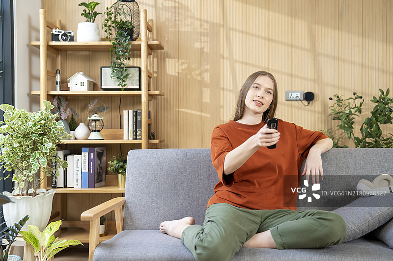 年轻女人坐在沙发上看电视，享受居家时光图片素材
