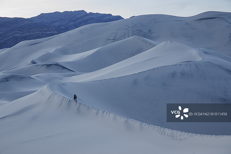 一位摄影师站在加利福尼亚州死亡谷的尤里卡沙丘的沙峰上，正值蓝色时刻。图片素材
