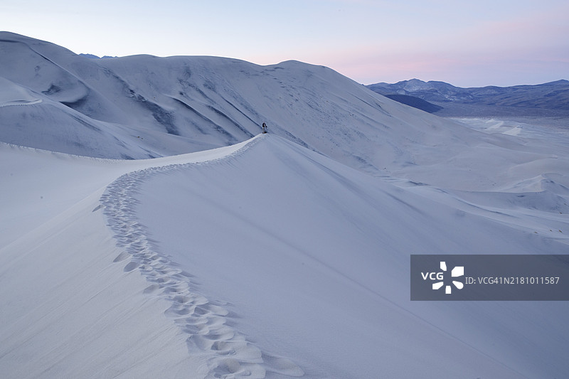 一位摄影师站在加利福尼亚州死亡谷的尤里卡沙丘上，蓝色时刻的沙丘顶峰。图片素材