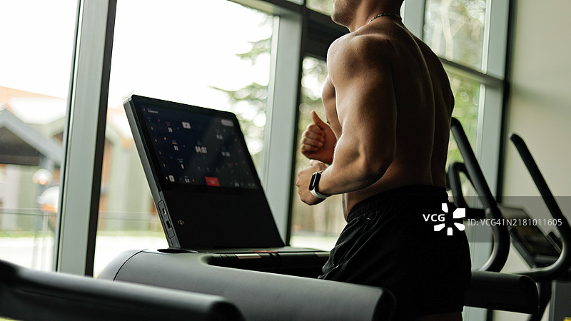 在健身房跑步机上赤膊跑步的健壮男人，健身爱好者进行有氧运动和耐力训练图片素材