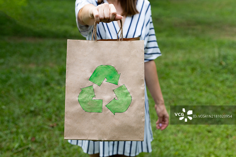 年轻女性手持环保包装，背景是一片绿色草坪，回收利用图片素材