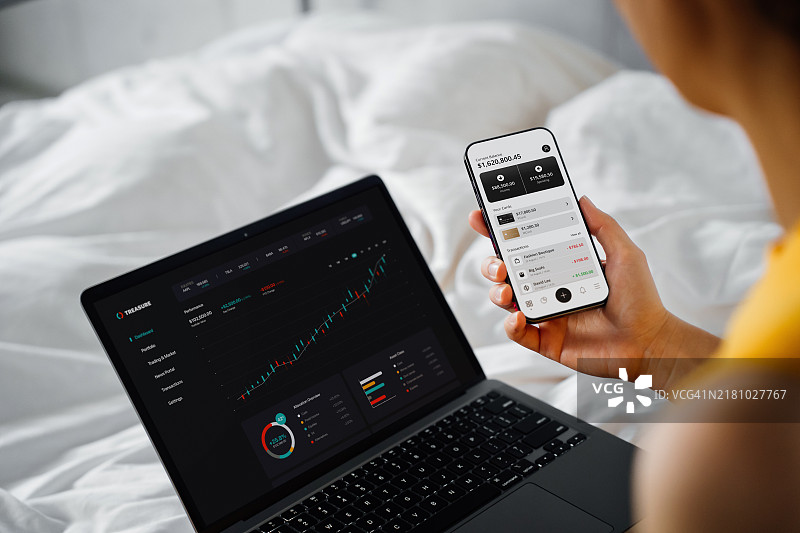 亚洲女性在线管理金融投资，分析股市交易，用笔记本电脑和智能手机制定财务计划的肩上视角。数字银行。财富管理。银行、金融和投资图片素材