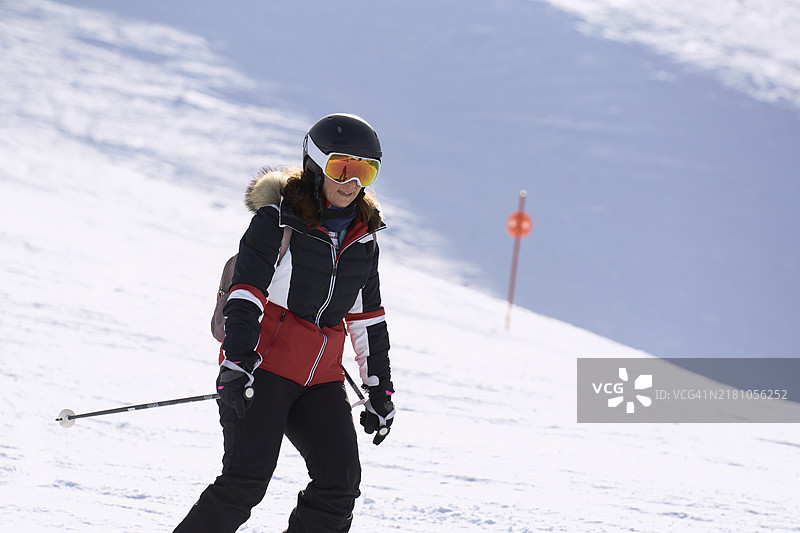 一位女性正在滑雪，沿着被雪覆盖的山坡下滑，穿着特殊的滑雪服，戴着护目镜，沐浴在阳光下。图片素材