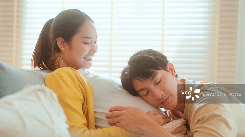 期待中的夫妻在阳光明媚的房间里分享快乐时光，伴侣与孕肚交谈。图片素材