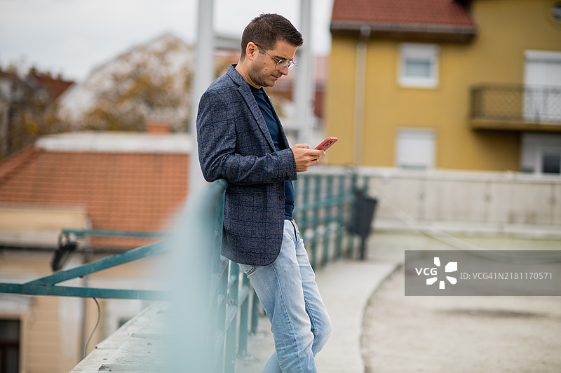 男人在城市环境中靠在栏杆上使用智能手机图片素材