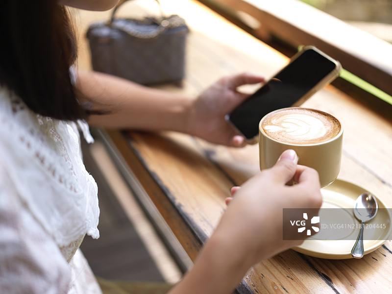亚洲女性在咖啡店里喝着咖啡，查看连接到免费WiFi的智能手机上收到的短信。图片素材