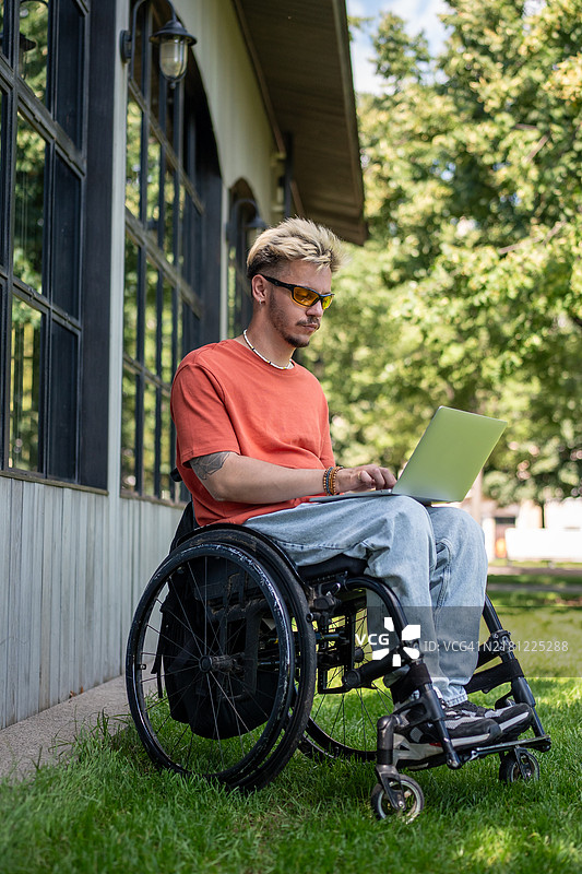 专注的轮椅男士在公园里使用笔记本电脑编程，享受新鲜空气。图片素材