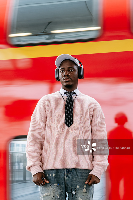 黑人男子在户外等火车，有色人种使用无线耳机听音乐和交流。以英俊的人和公共交通工具为主题的生活方式摄影。图片素材