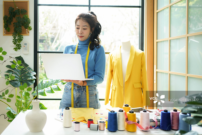 年轻女性时装设计师在展厅里使用笔记本电脑工作，接收客户的定制设计订单。图片素材
