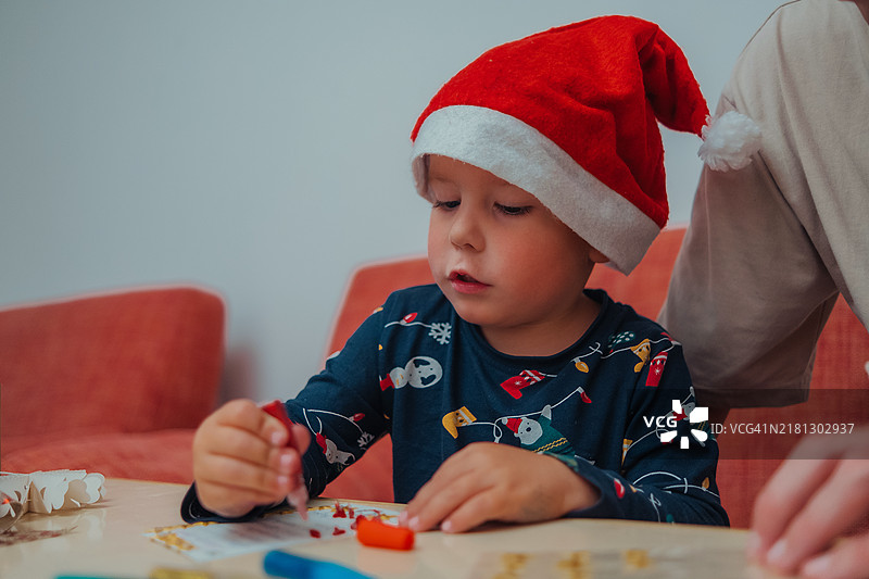 为圣诞节做准备的一家人。父子俩坐在家里的沙发上，一起给圣诞老人写信。孩子正在装饰卡片。图片素材