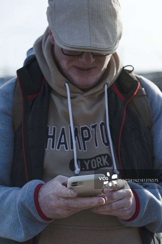 成熟男性戴着帽子，近距离肖像，正在使用智能手机。图片素材