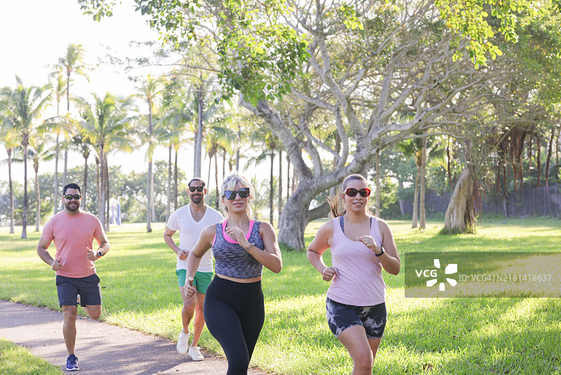 一小群拉丁裔千禧一代的人穿着运动服在公园里一起跑步。图片素材