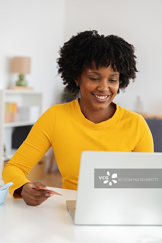 微笑的女性在家中使用笔记本电脑和信用卡进行在线购物图片素材