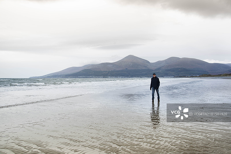 男子在银色天空和金色沙滩的沙滩上行走图片素材