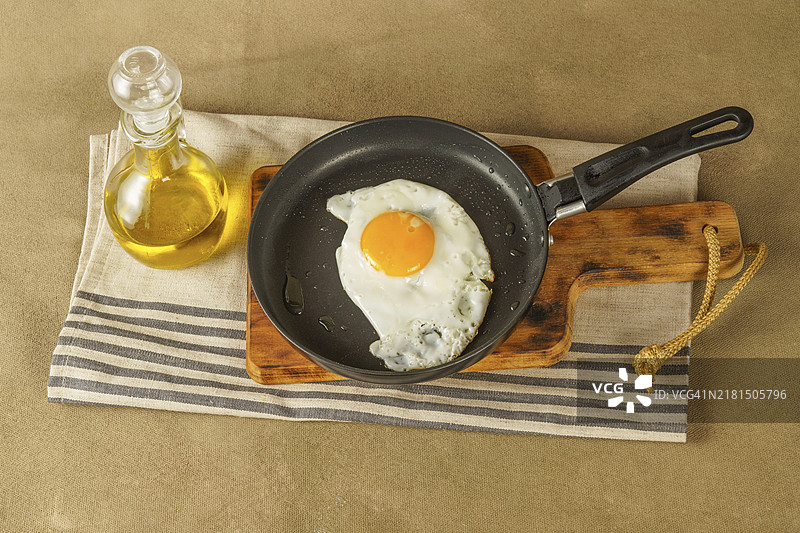平底锅煎鸡蛋配特级初榨橄榄油，木板上放玻璃油瓶图片素材
