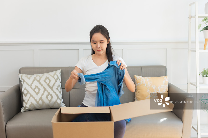 年轻的亚洲女性打开从网上商店收到的衣服。接收、打开并尝试在线购买的概念。图片素材