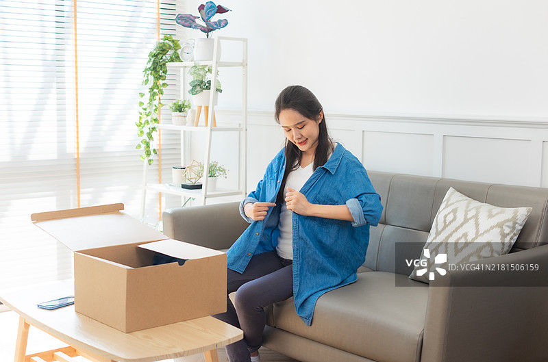 年轻的亚洲女性打开从网上商店收到的衣服。接收、打开并尝试在线购买的概念。图片素材