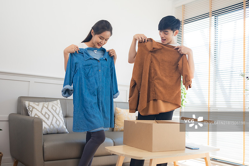 年轻的亚洲夫妇打开从网上商店收到的衣服，接收并打开网购的概念图片素材