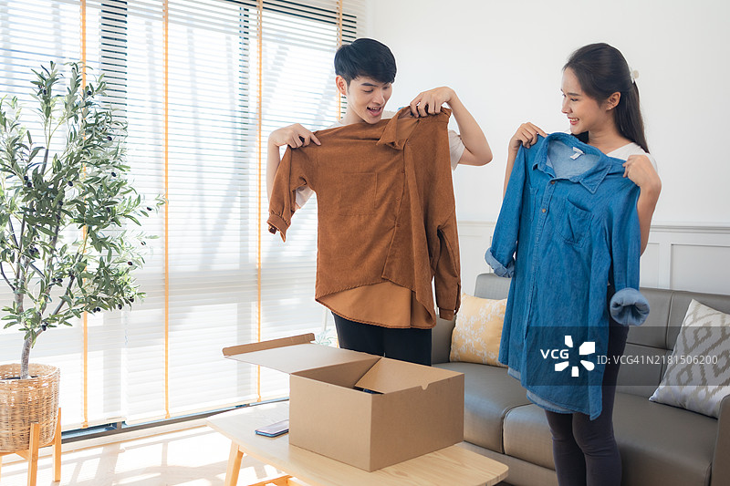 年轻的亚洲夫妇打开从网上商店收到的衣服，接收并打开网购的概念图片素材