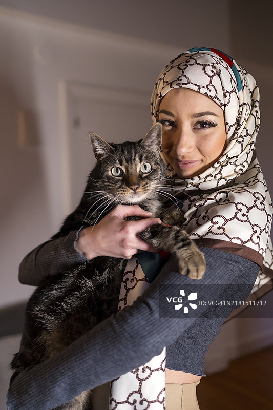 戴着面纱的阿拉伯女孩和可爱的猫咪在家里的肖像图片素材