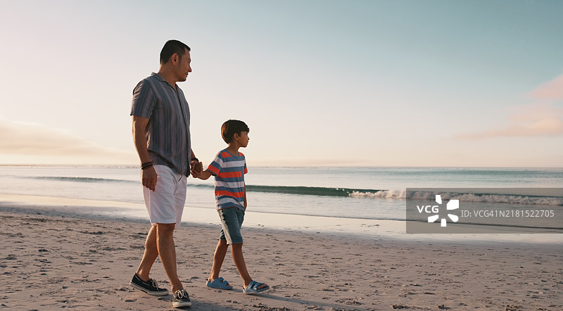 父亲和儿子在沙滩上手牵手散步，享受充满爱意的亲子假期图片素材