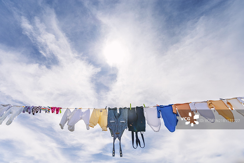 许多婴儿服装挂在蓝色多云的天空下图片素材