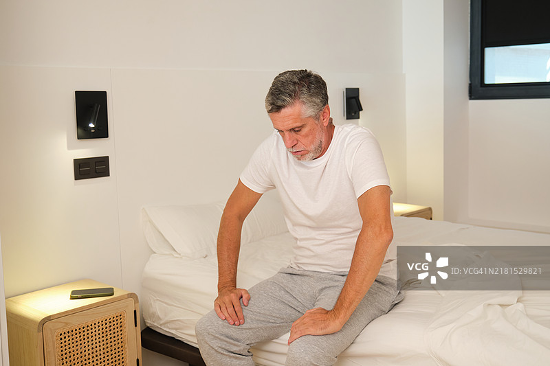 年长的男人坐在卧室的床上感到膝盖疼痛图片素材
