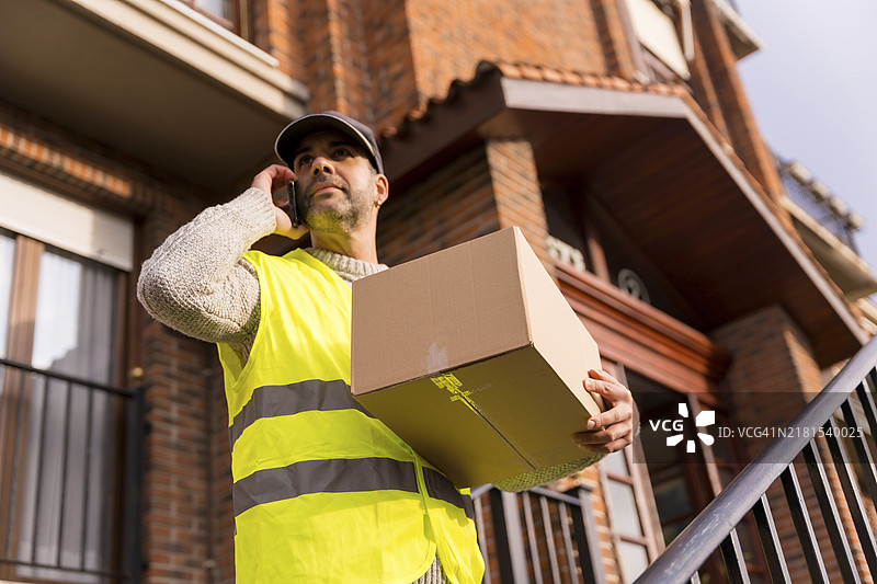 在线商店的包裹递送员在房屋楼梯上呼叫顾客图片素材