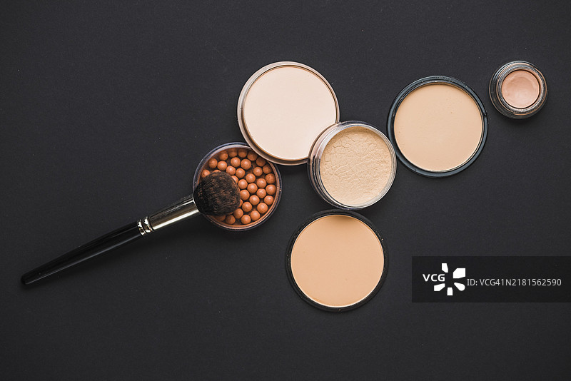黑色背景上的古铜色珍珠蜜粉和化妆刷图片素材