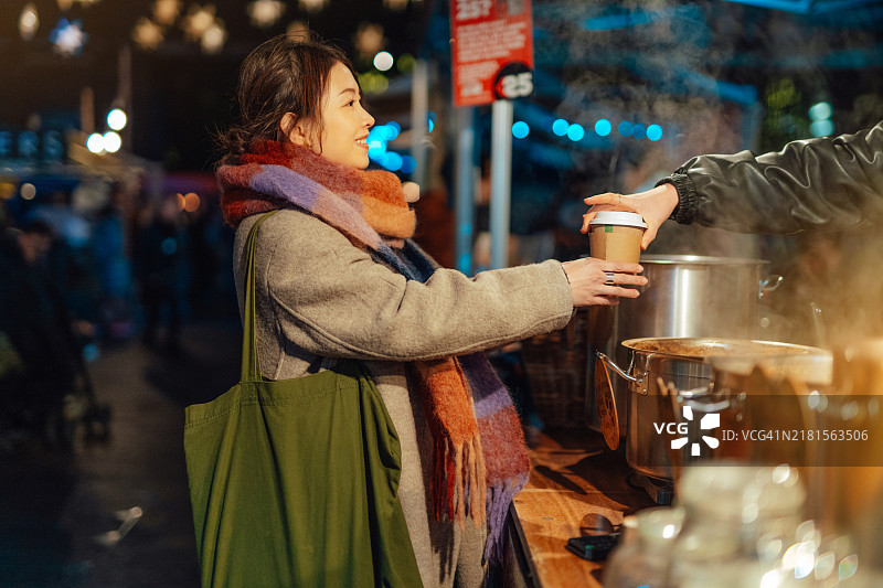 年轻的亚洲女性在圣诞市场的摊位上购买热红酒图片素材