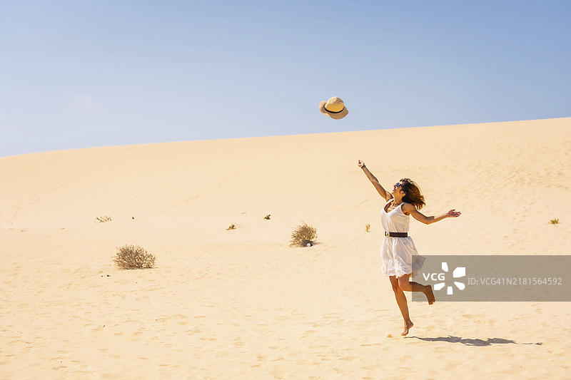 在西班牙富埃特文图拉岛科拉雷侯自然公园沙丘上，兴奋地向上扔帽子的游客图片素材