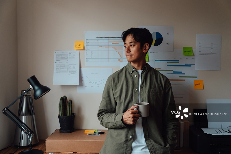 思考中的亚洲男子在家工作时享受咖啡休息。图片素材