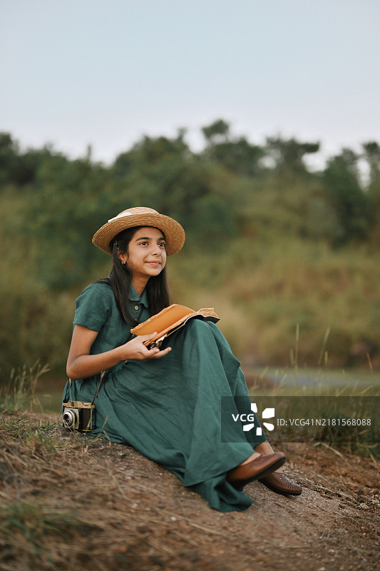 女孩穿着复古裙子，戴着草帽，在大自然中阅读书籍图片素材