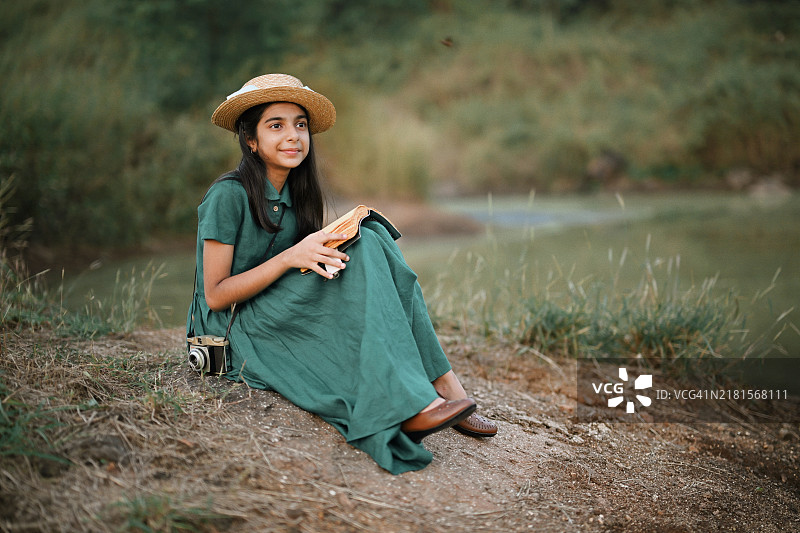 女孩穿着复古裙子，戴着草帽，在大自然中阅读书籍图片素材
