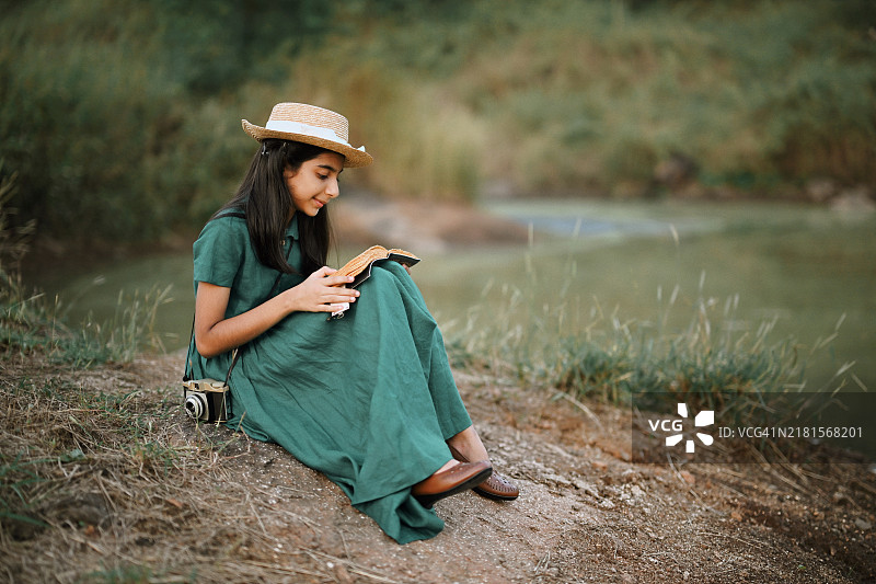 女孩穿着复古裙子，戴着草帽，在宁静的大自然中阅读书籍图片素材
