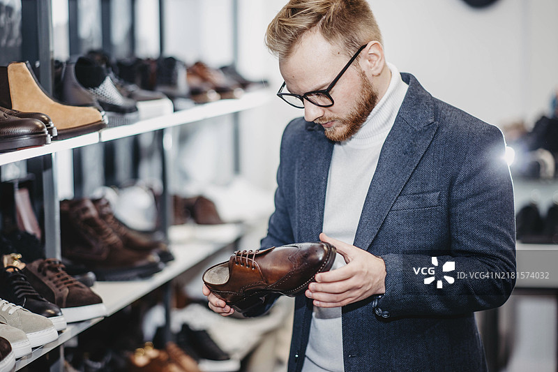 戴眼镜和夹克的时尚男造型师在商店里挑选鞋子图片素材