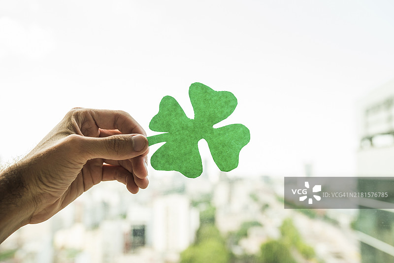 手持绿色纸质三叶草，城市景观图片素材