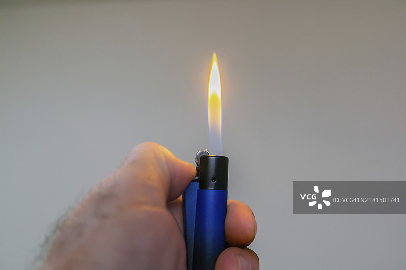 男人的手点燃一个蓝色打火机，有复制空间和浅色背景图片素材