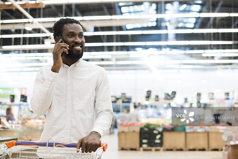 快乐的黑人男子在购物时用手机交谈图片素材