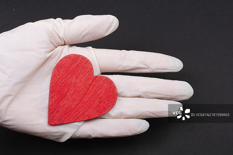 戴无菌手套的手捧着一颗心，健康护理概念图片素材
