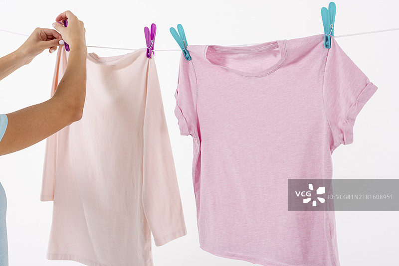 女人用衣夹将T恤固定在晾衣绳上图片素材